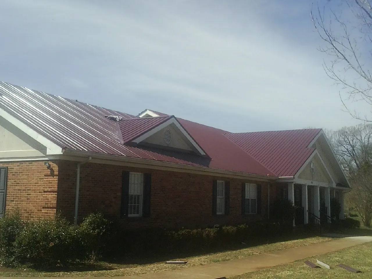 Red metal roof with gabled entries on a long brick building, from a Hail Damage Roof Repair job in Powell Butte