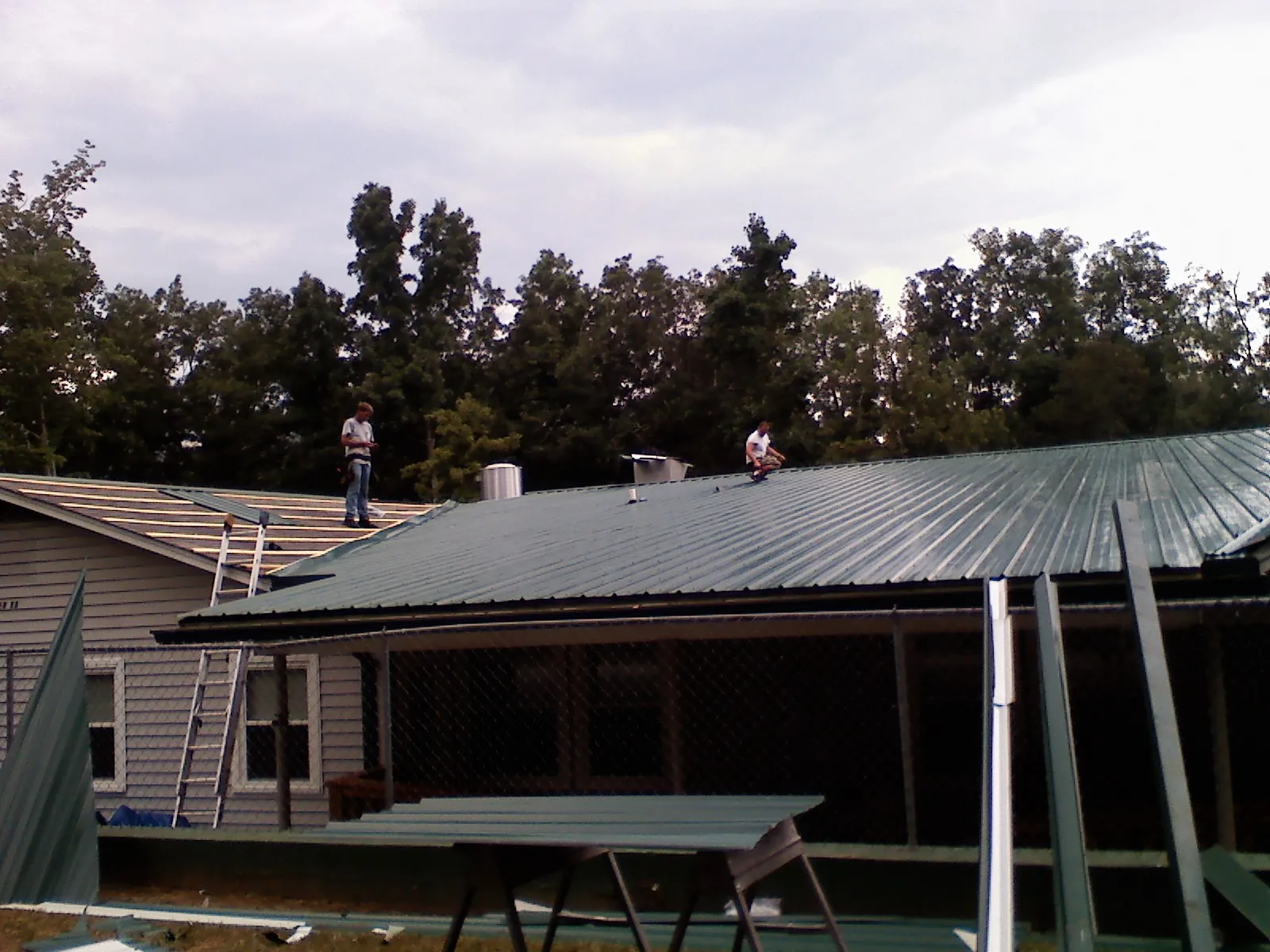 Two roofers installing green metal panels above a covered porch in Powell Butte
