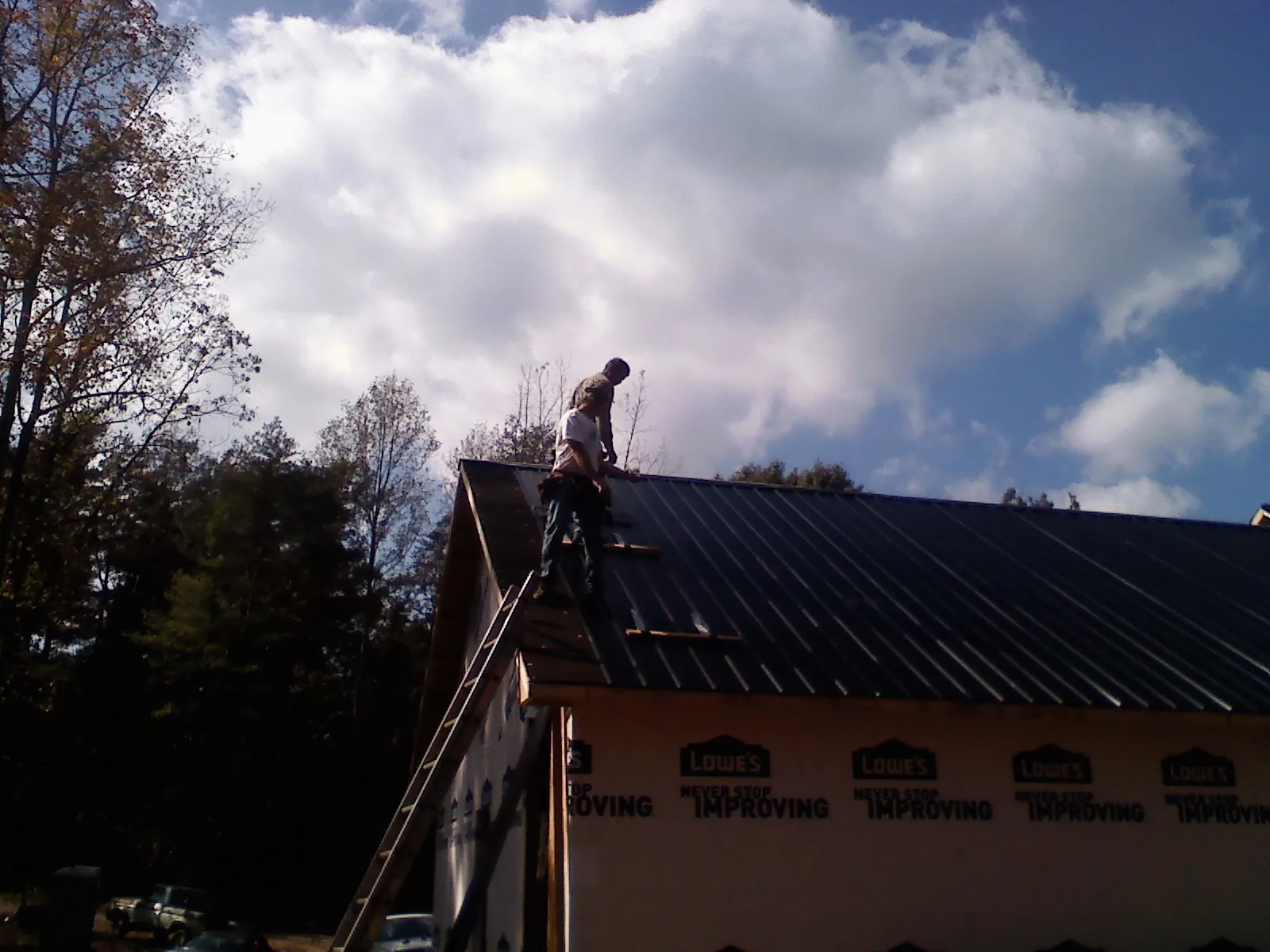 Roofer fastening dark metal panels high against a cloudy sky, from a Roof Inspection job in Powell Butte