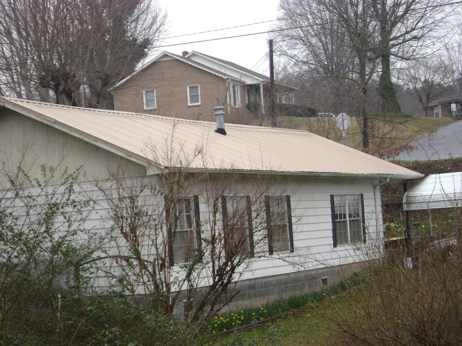 Tan metal roof on a white sided house set into a hillside — Commercial Roofing by Roofing Brothers in Powell Butte
